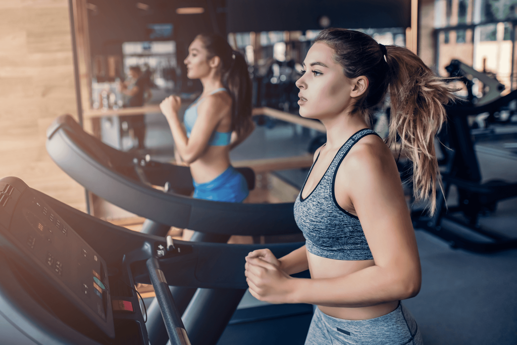 Side view of two sports women on running on a treadmill.